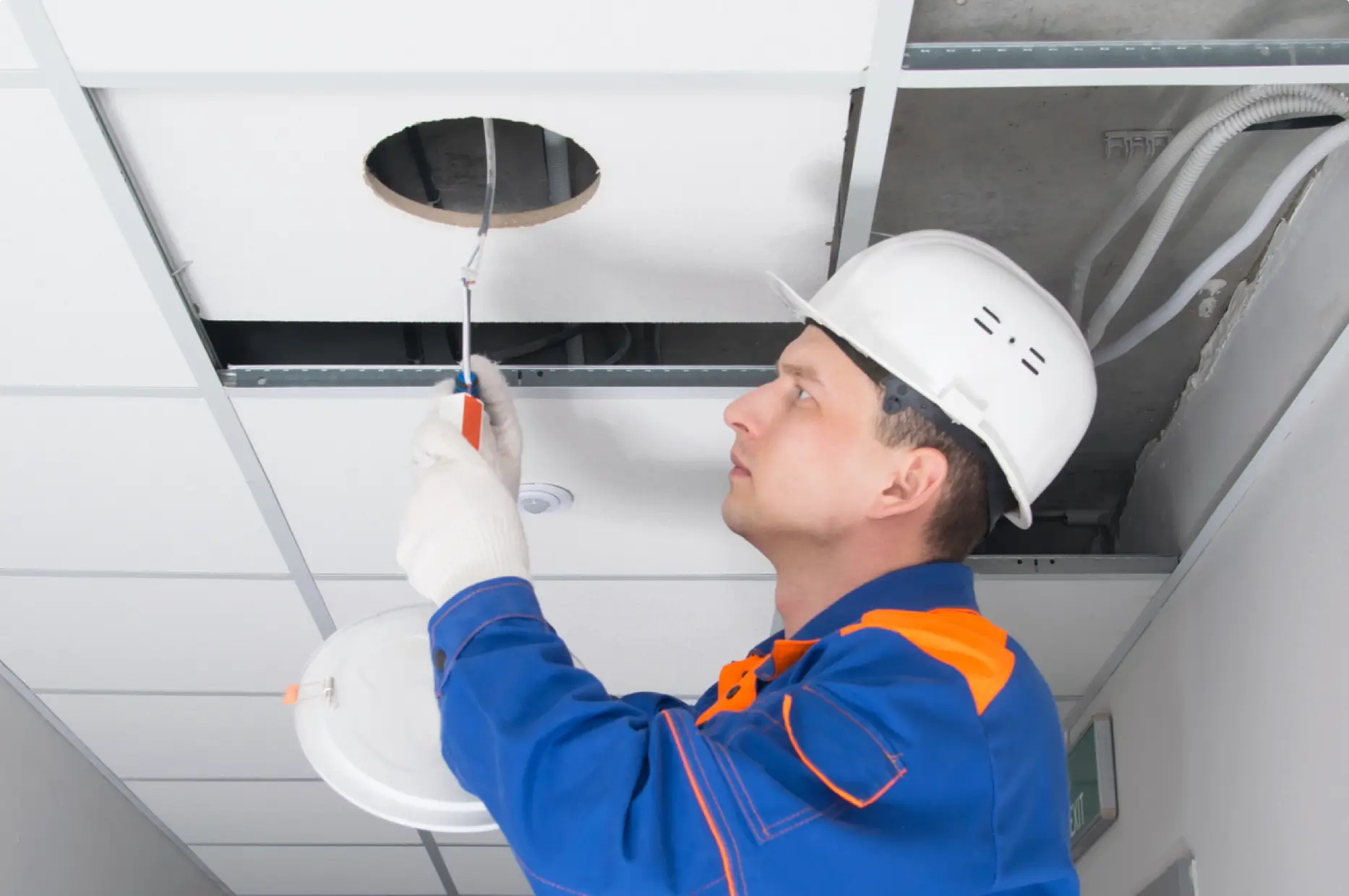Electrician performing lighting maintenance in ceiling tiles