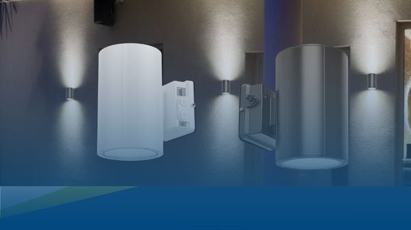 Two modern cylindrical wall sconces shown mounted on a wall, one with a white shade and one with a clear shade, each casting light downward. The image appears to be a composite or promotional render with a blue lower band and additional wall lights in the background.